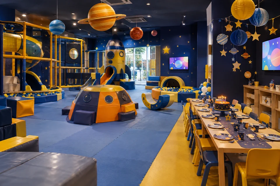 Sala de festas com mesa comprida posta, bolo com velas e planetas pendurados